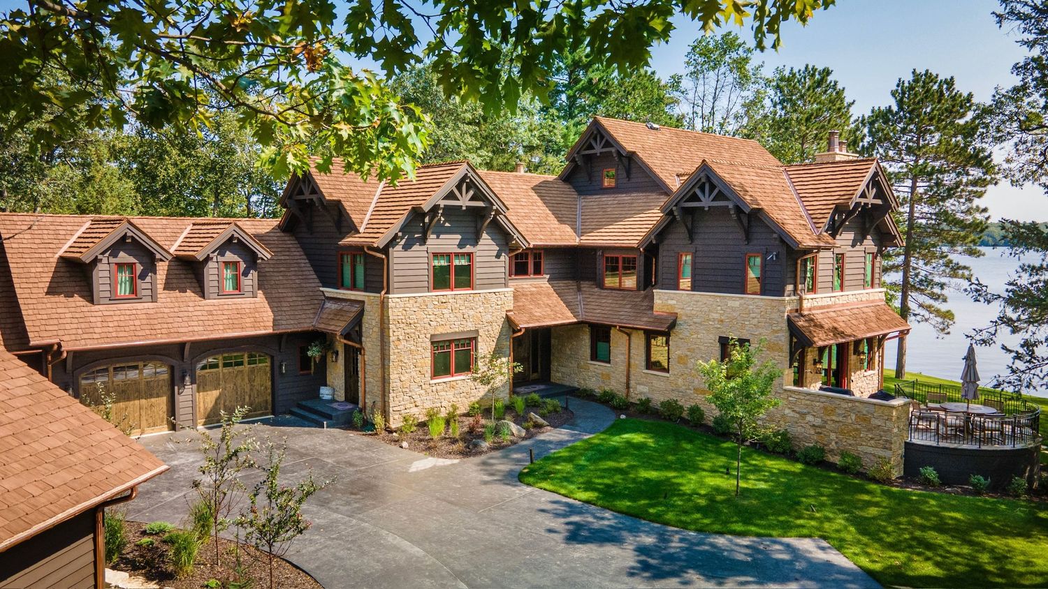 Aerial panoramic view of a luxury lakefront estate with stone and wood architecture surrounded by lush trees. Spencer WI