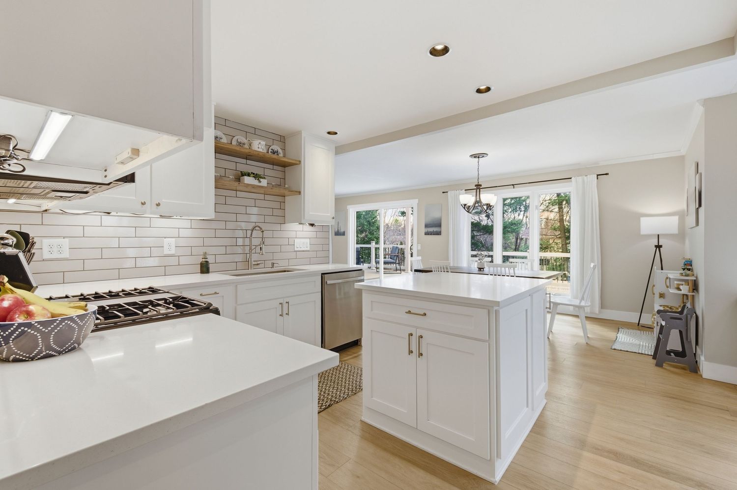 Bright white kitchen with island, subway tile backsplash, hardwood floors, and open view to sunlit living area.