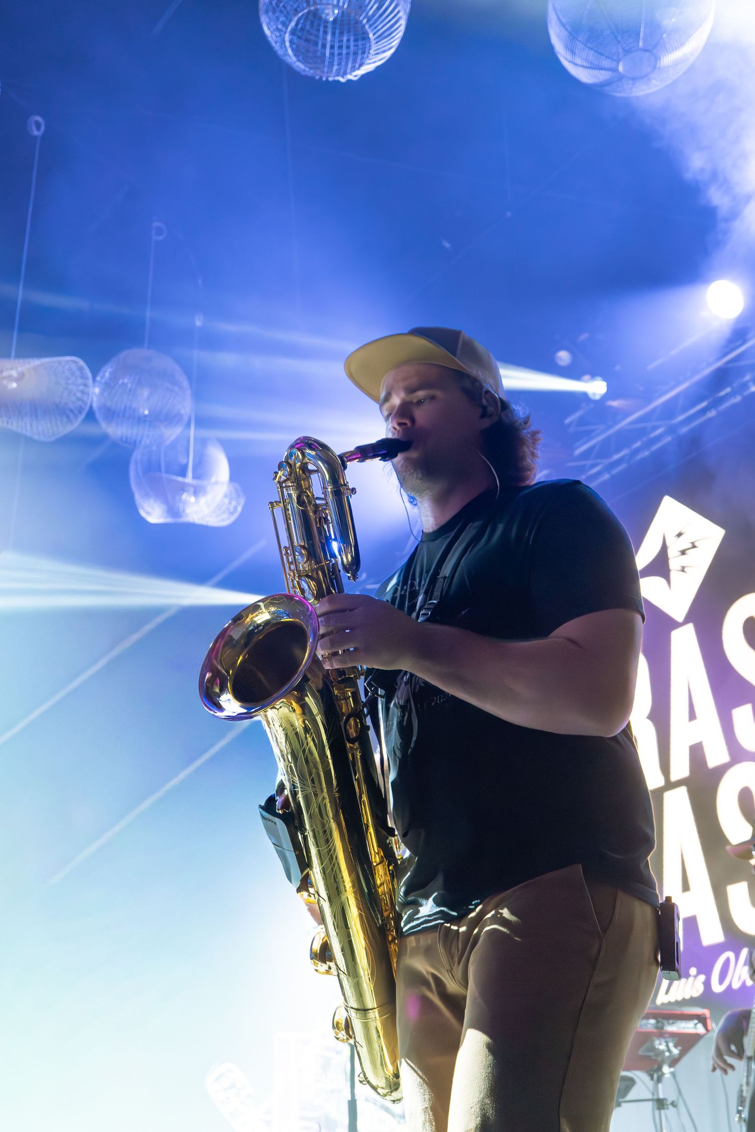 Musician in black performs with a saxophone on stage under blue concert lighting and disco balls.