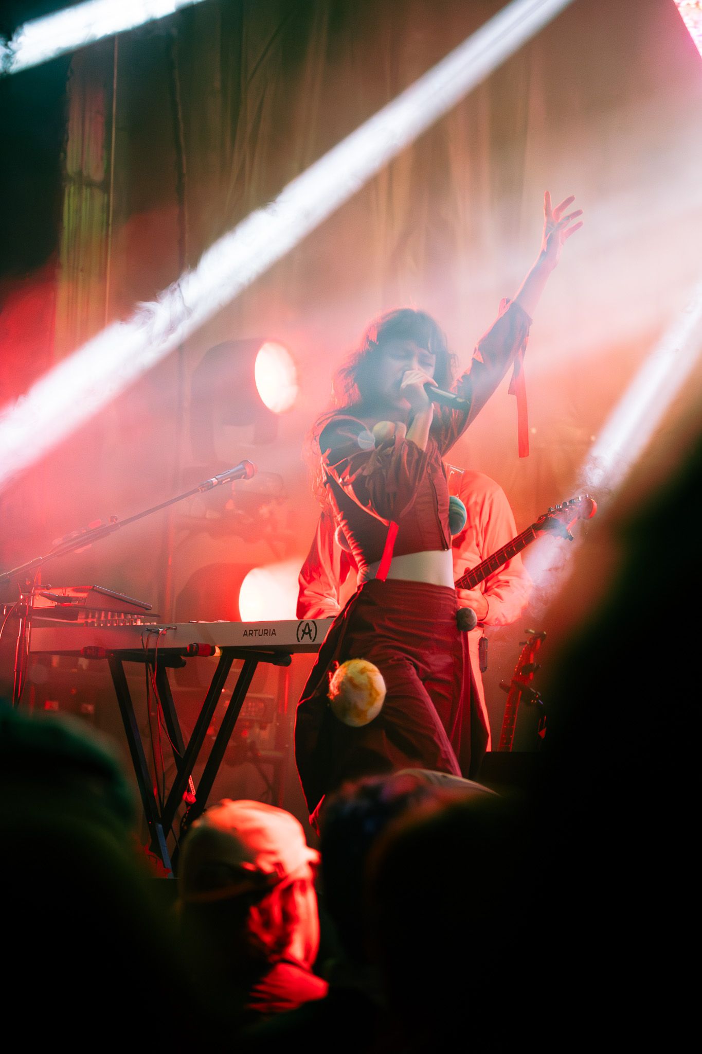 Female performer singing on stage with dramatic red lighting and raised arm at a live concert.