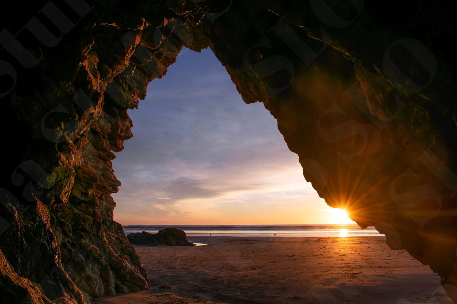 Natural rock arch frames a golden sunset over the ocean coastline.