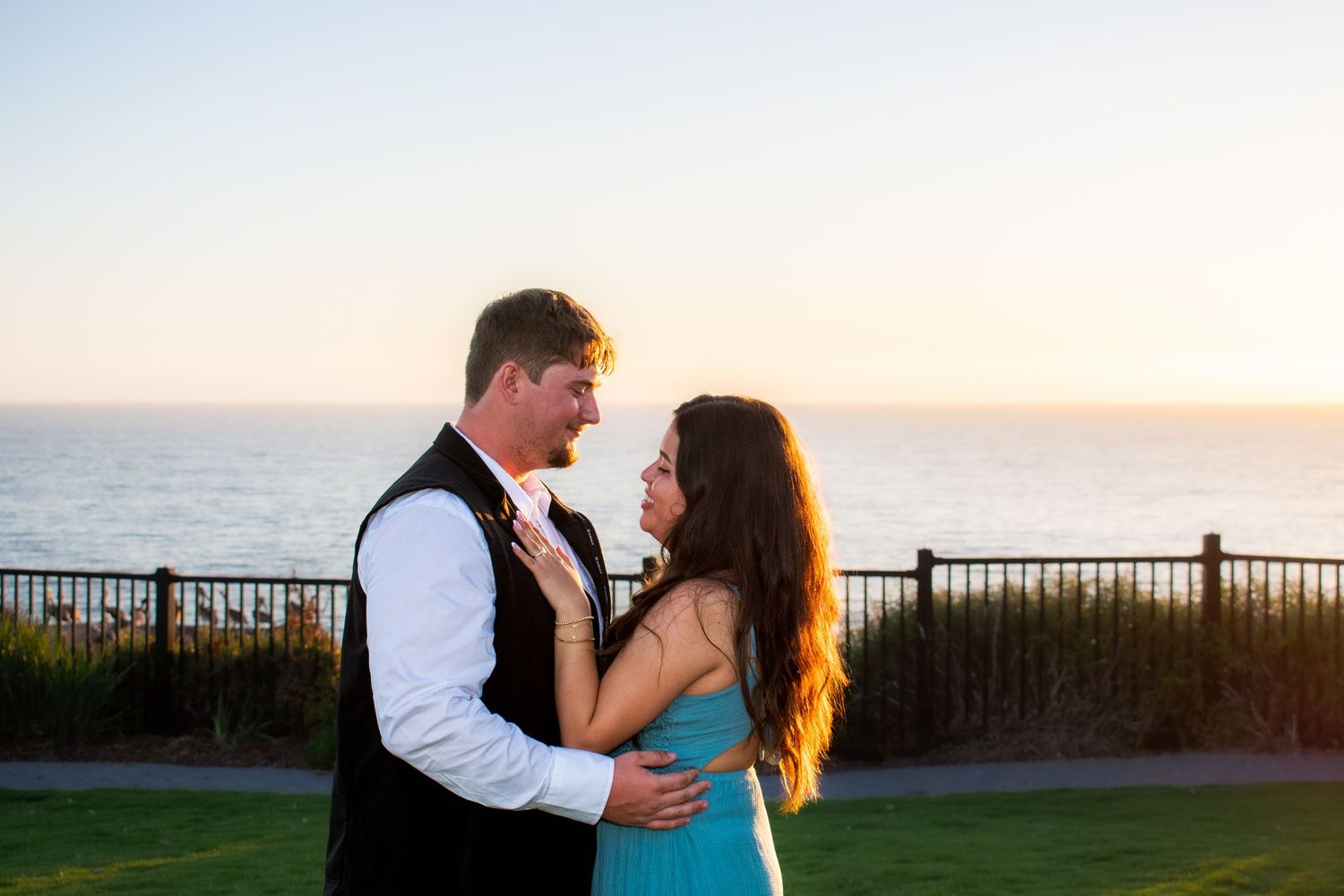 Couple embraces during golden hour photoshoot with ocean and palm trees in background.