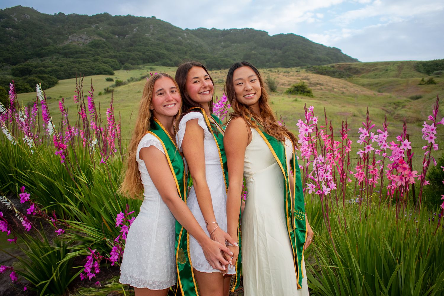 Bridesmaids in white dresses pose among purple wildflowers with mountains in background.