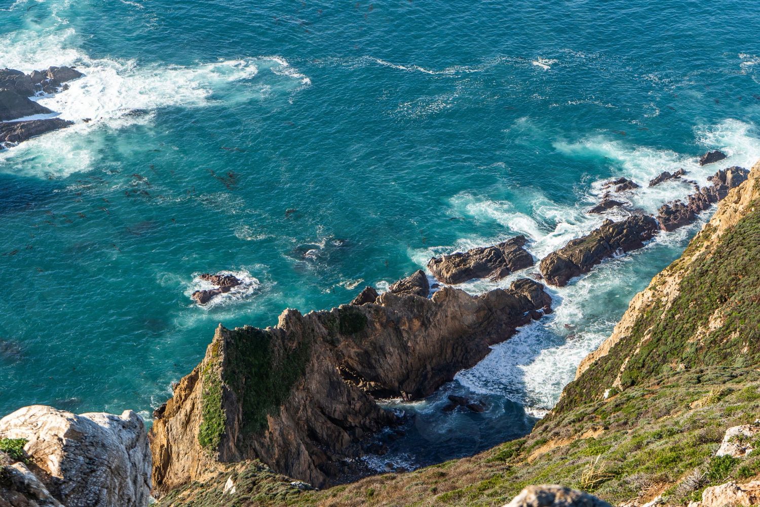 Aerial view of rugged coastal cliffs meeting turquoise ocean waves with rocky outcroppings along a scenic shoreline.
