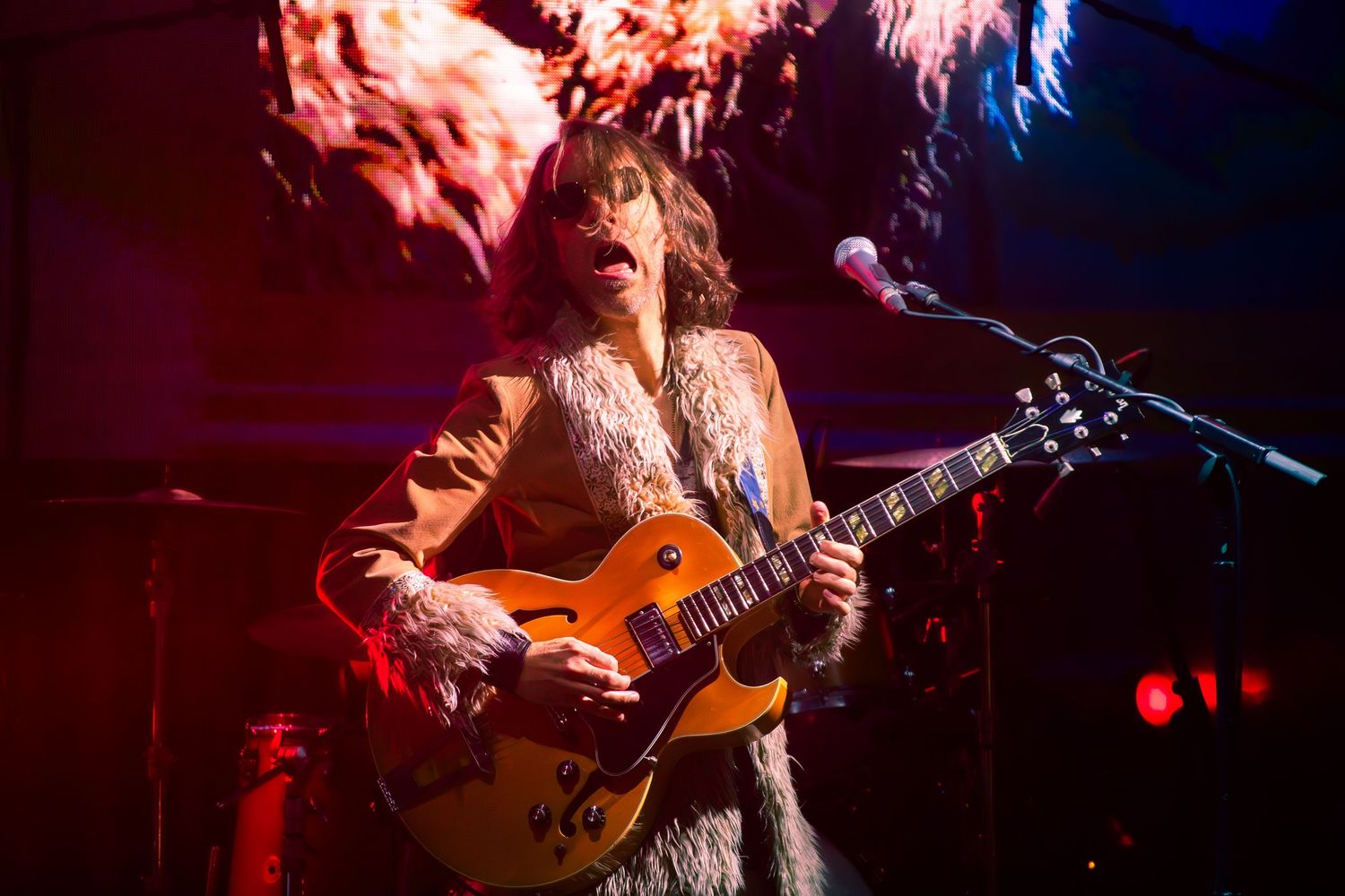 Electric guitarist performing on stage with dramatic red lighting during a concert performance.