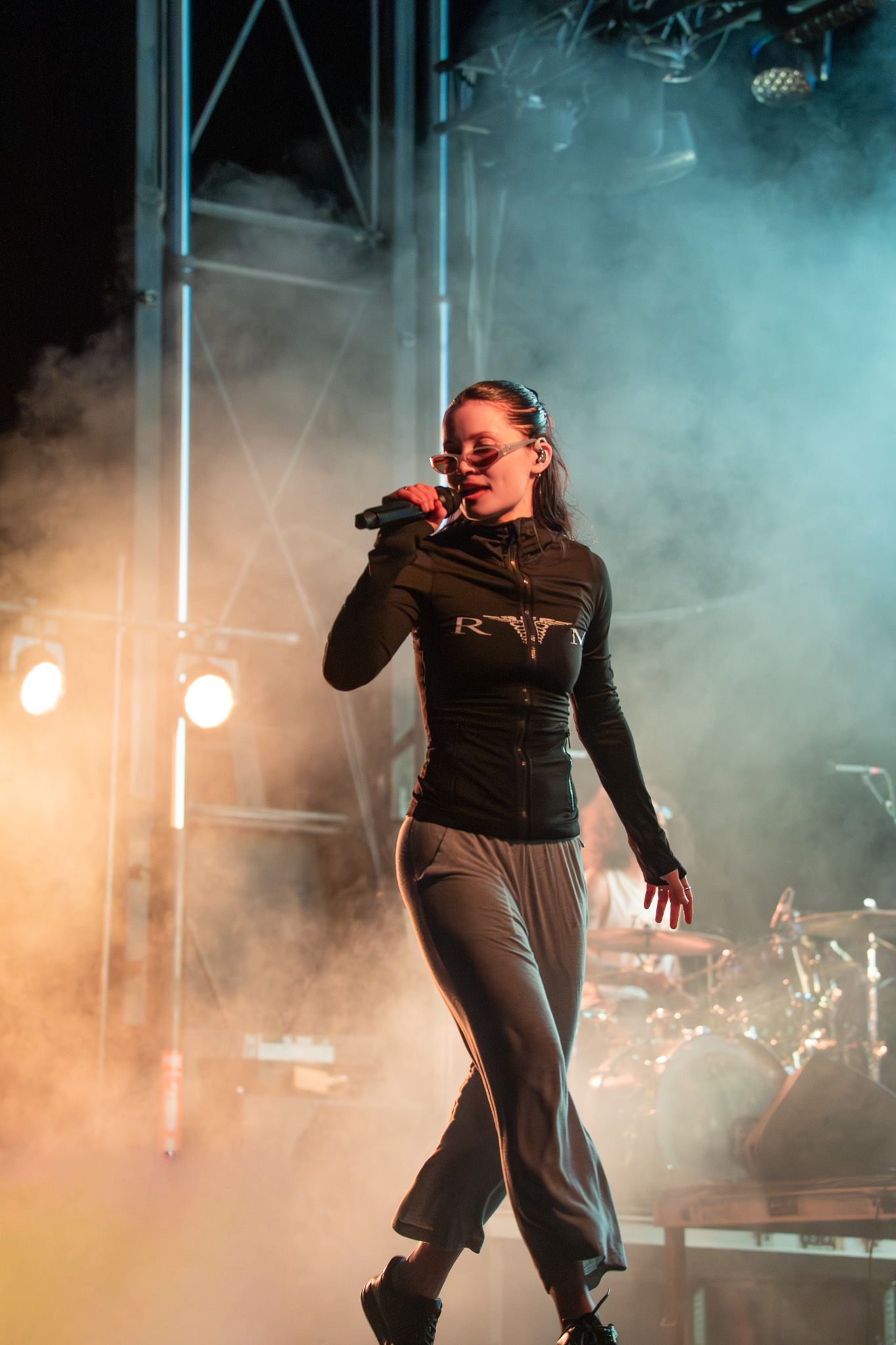 Female singer performing on stage with microphone, dramatic fog and stage lighting at live concert.
