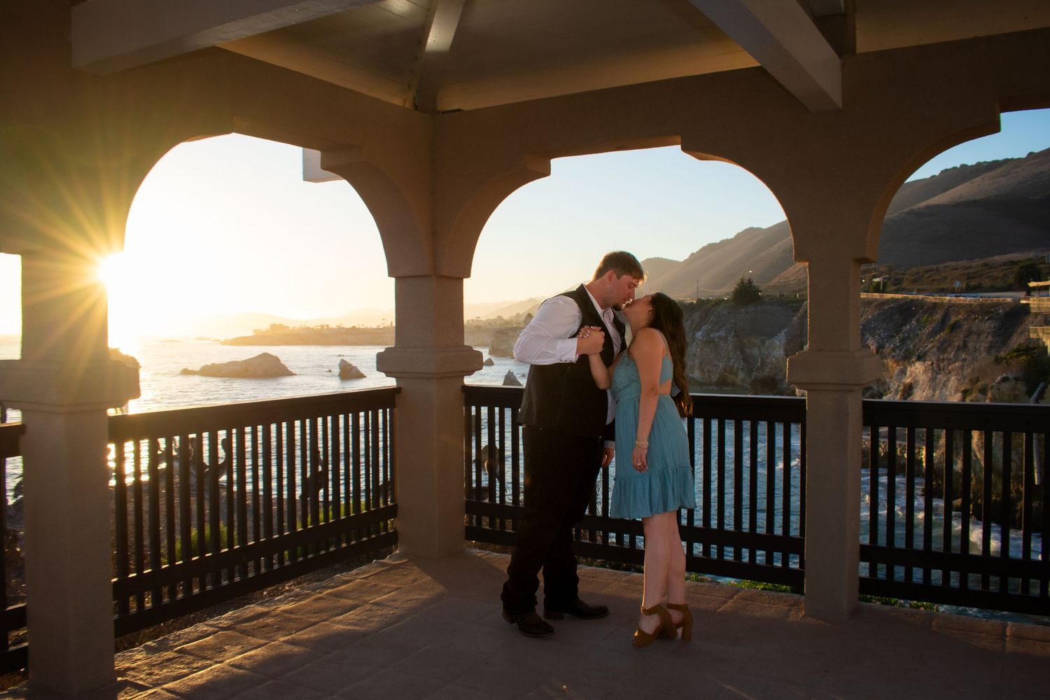 Covered terrace with arched columns overlooking coastal cliffs at sunset.