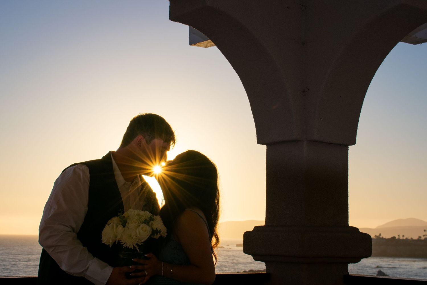 Romantic silhouettes against sunset through Mediterranean archways overlooking the sea.