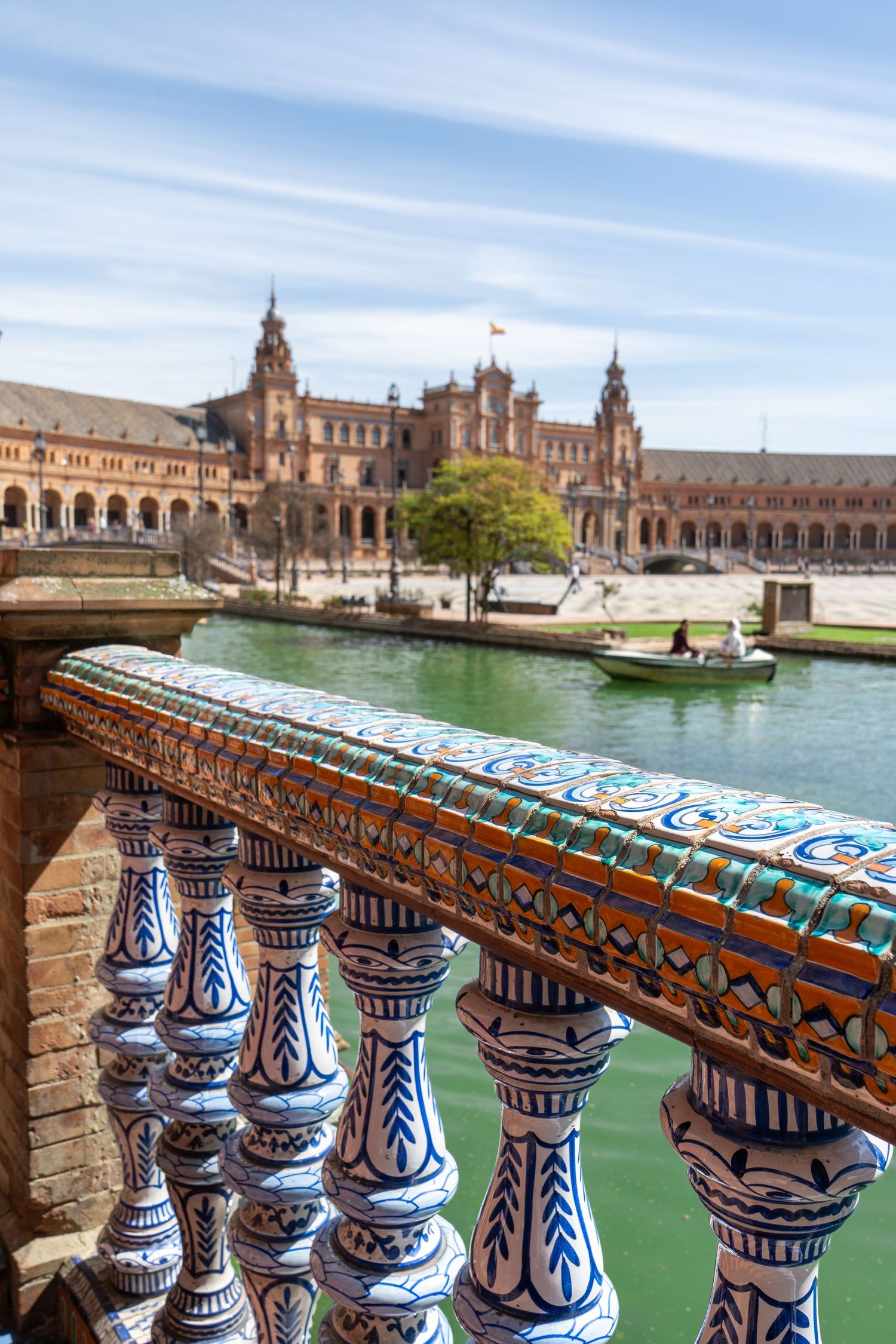 Ornate ceramic balustrade overlooking Plaza de Espana's green canal and historic Renaissance architecture in Seville, Spain.