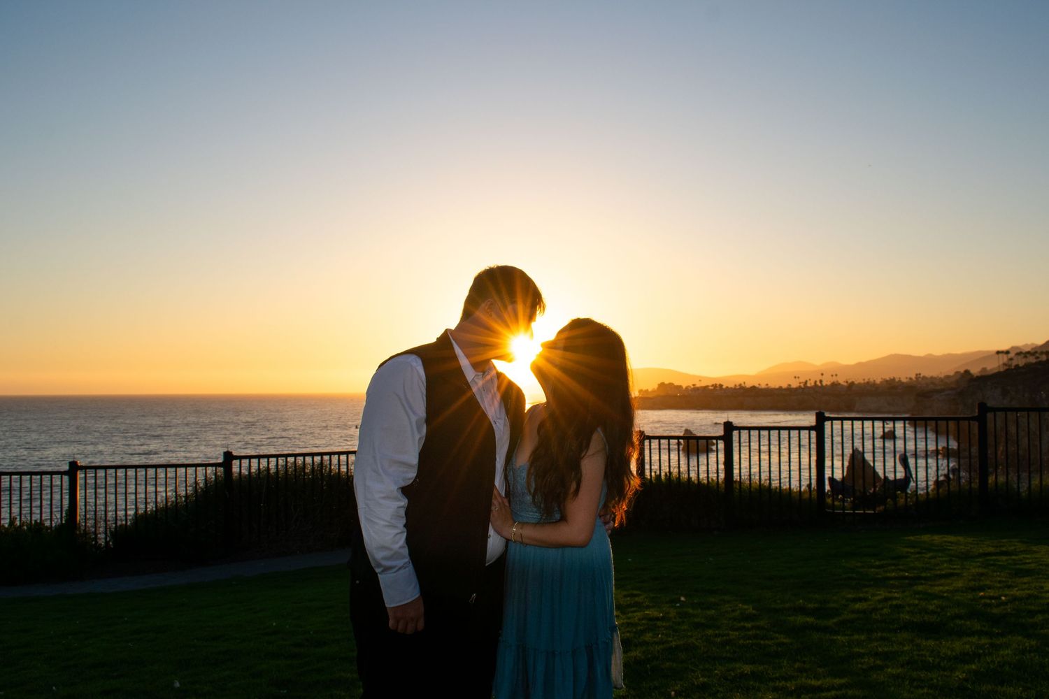 Silhouetted couple shares intimate moment against vibrant sunset sky by the ocean.