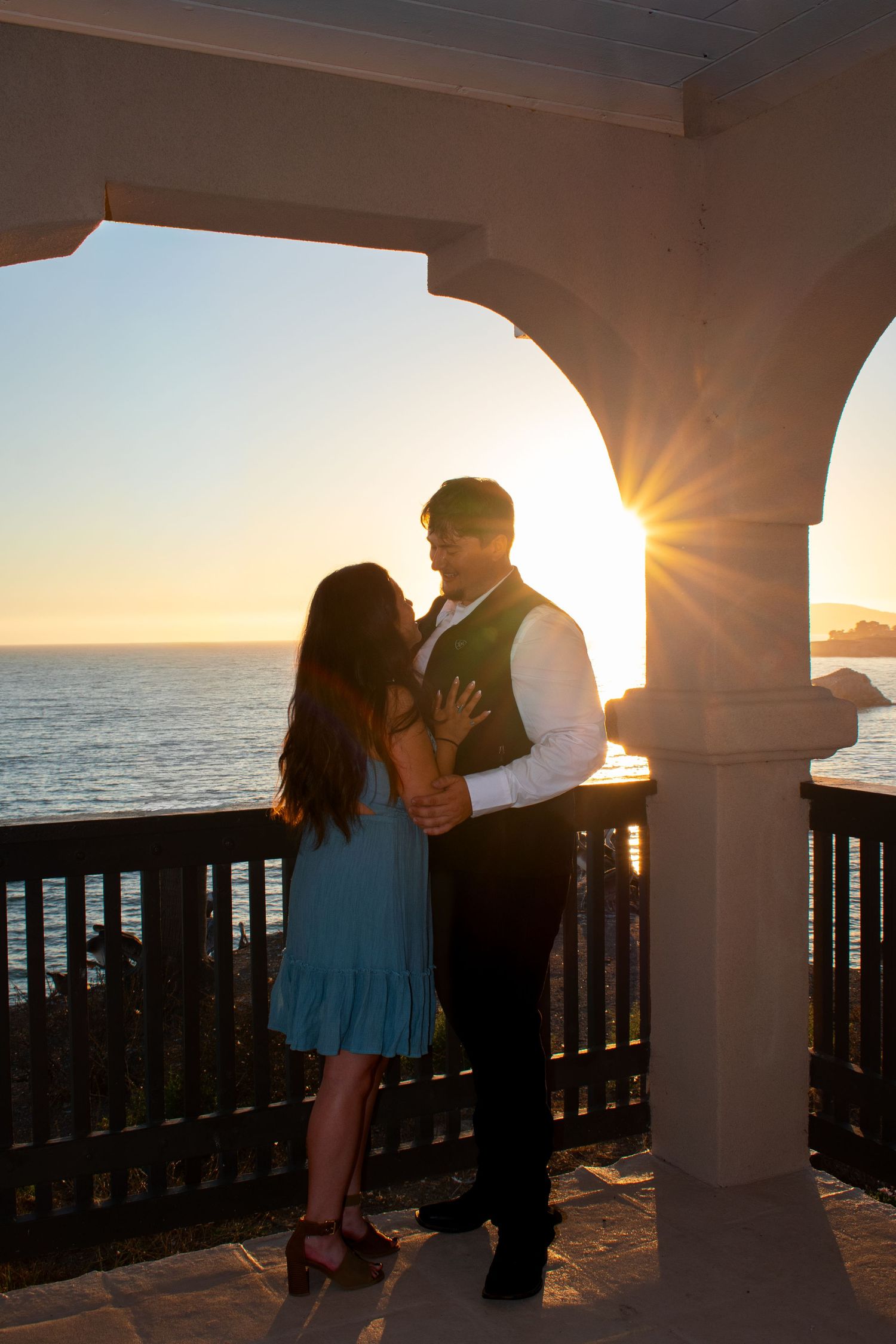 Silhouetted couple sharing an intimate moment on a seaside terrace during golden hour.