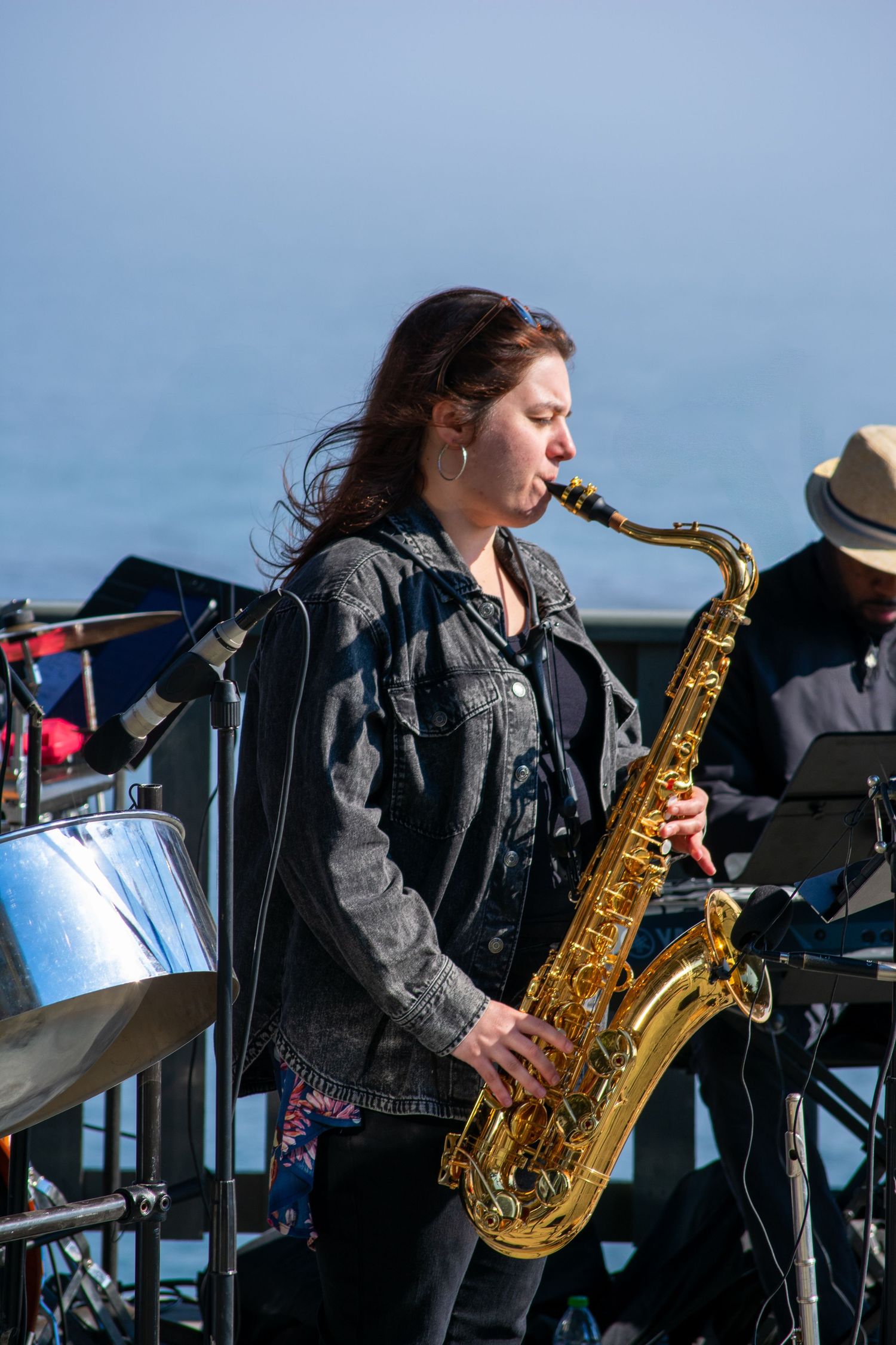 Saxophone player in denim jacket performs during outdoor concert with ocean view.