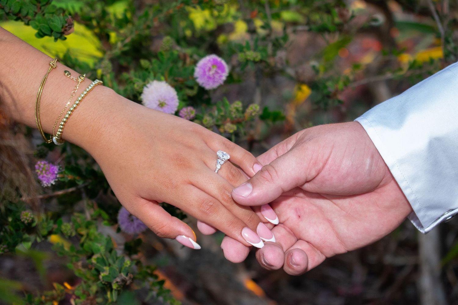 Close-up shots of hands displaying engagement ring in garden with flowers.