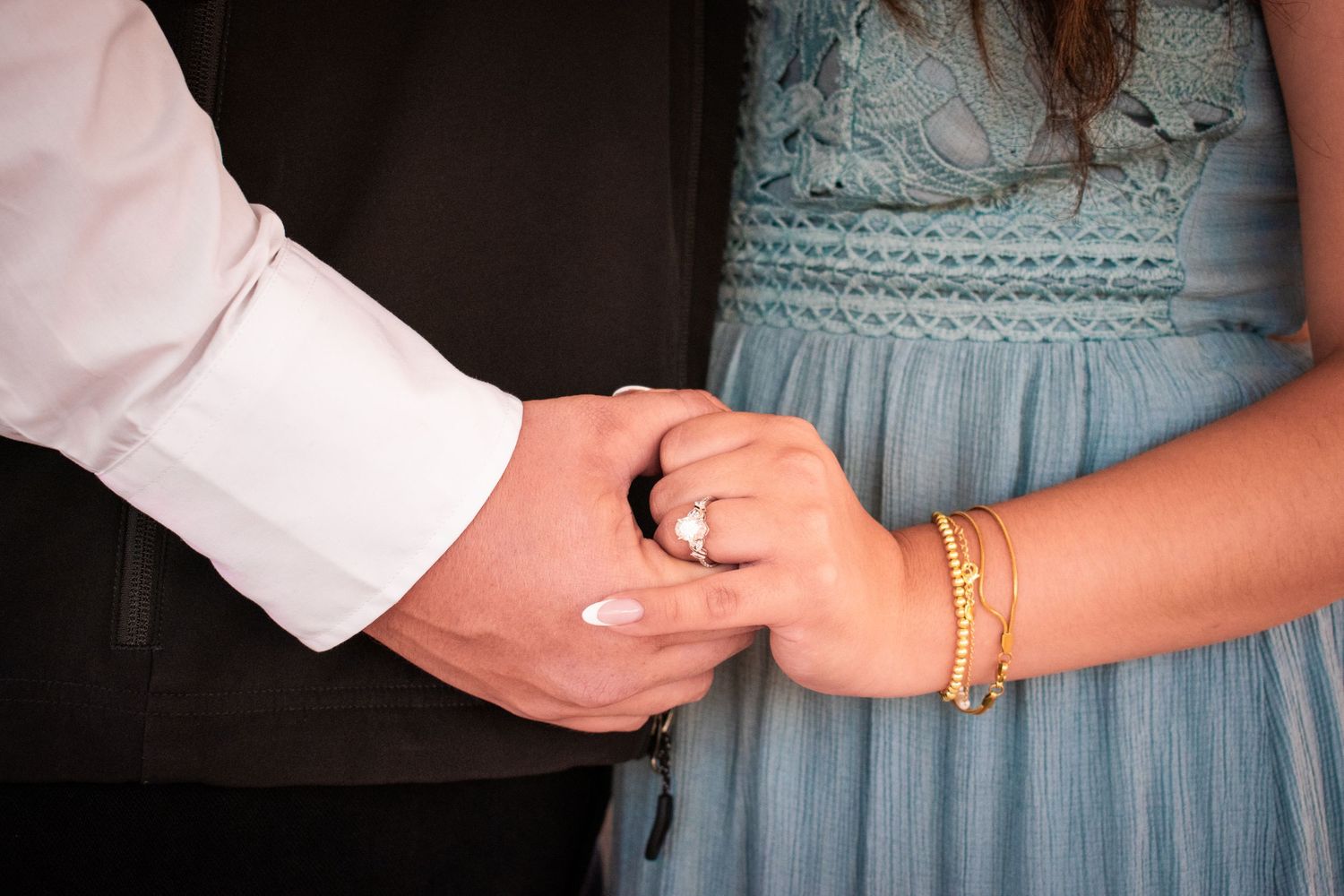 Close-up of hands wearing elegant jewelry against a light blue dress fabric.