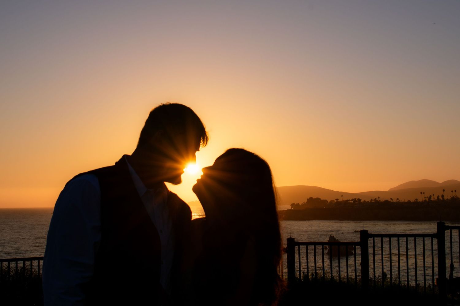 Dramatic silhouette of couple against orange sunset sky with ocean horizon.