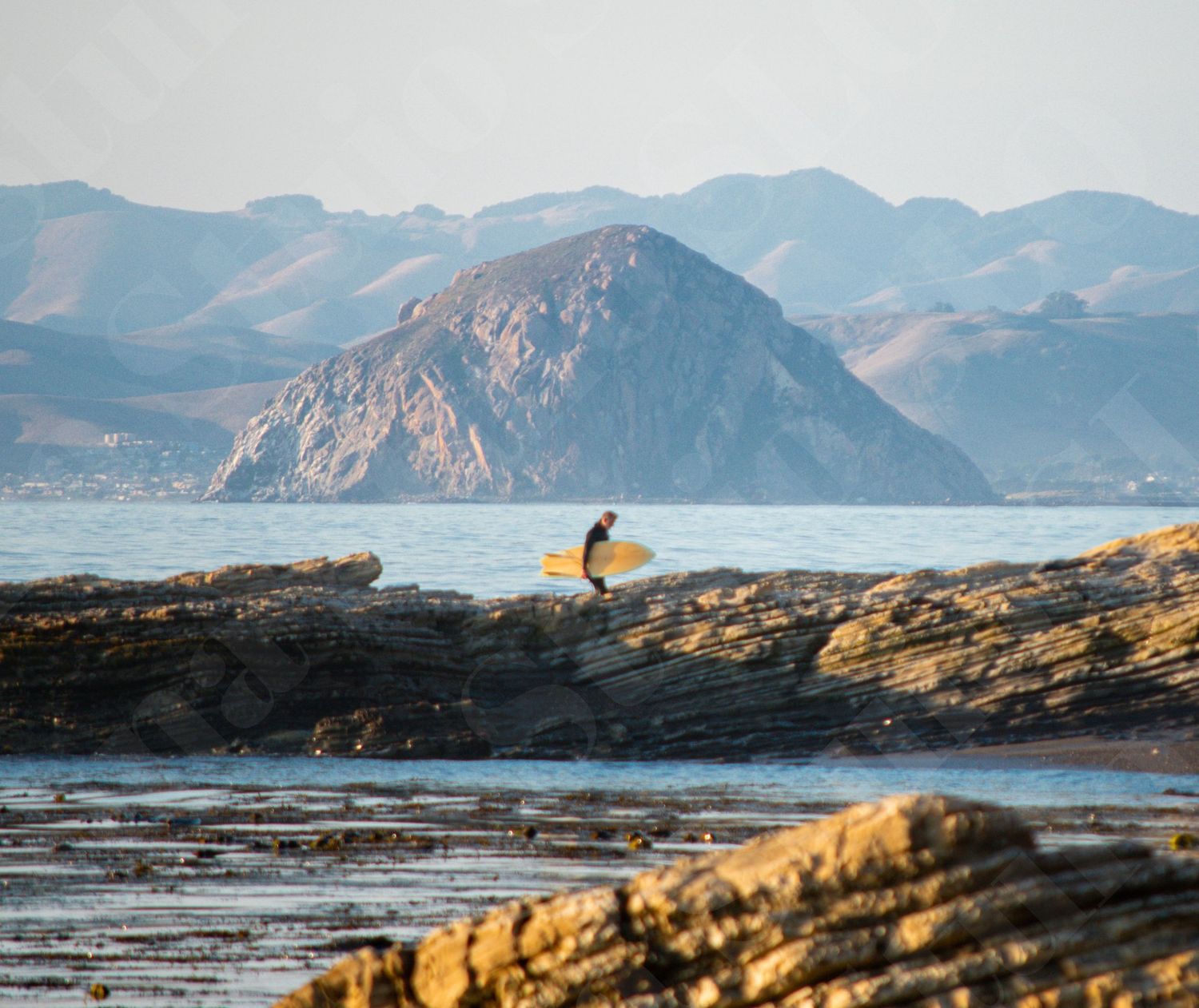 Rocky coastline with dramatic mountain peaks rising above the ocean during golden hour.