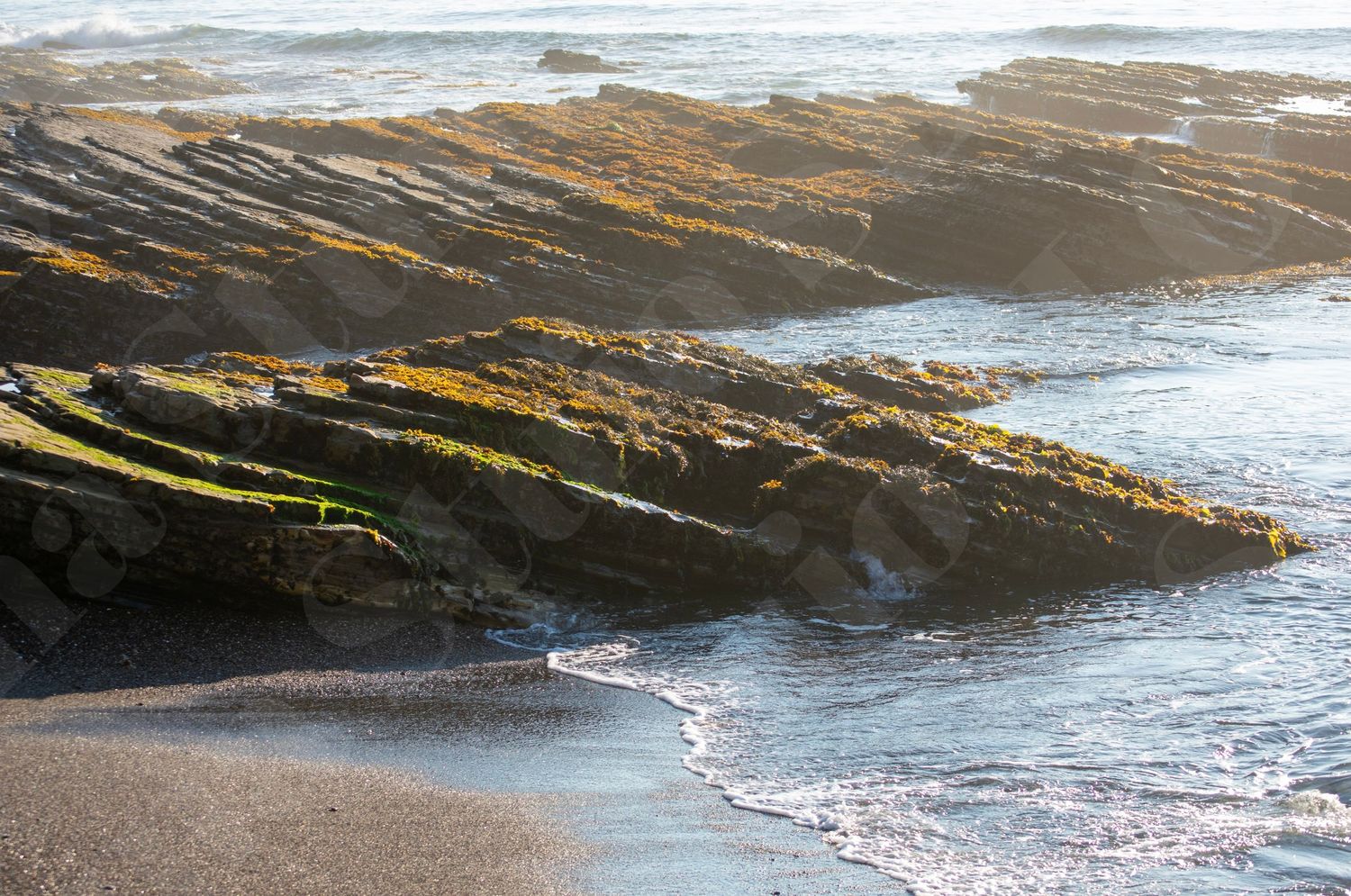 Striped rock formations meet the ocean waves along a rugged coastline.