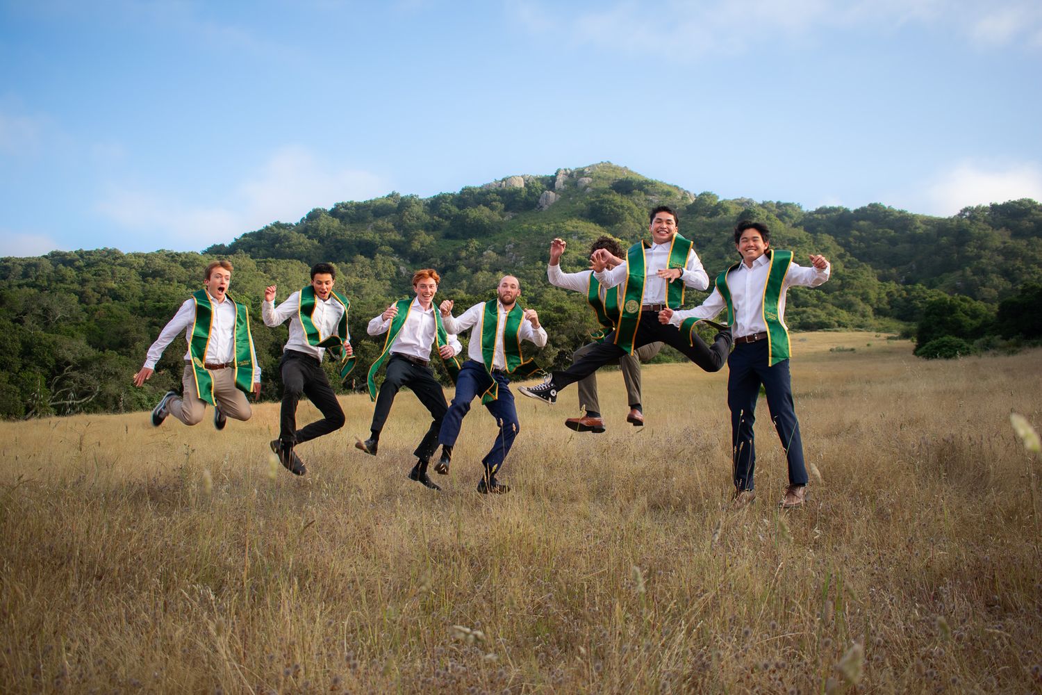 Wedding party performs synchronized jumping pose in golden field.