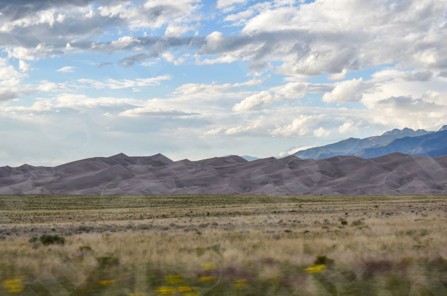 Panoramic desert landscape with distant mountain ranges under scattered clouds.