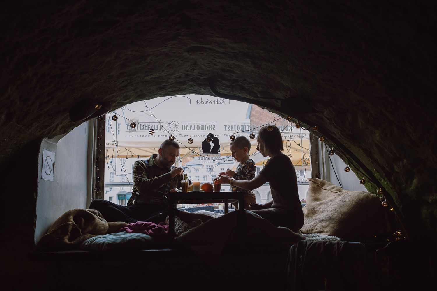 Silhouetted figures gathered around table seen through dark window frame.