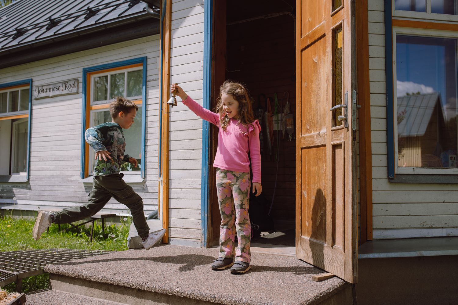 Children enter and exit through wooden doors of a traditional schoolhouse building.