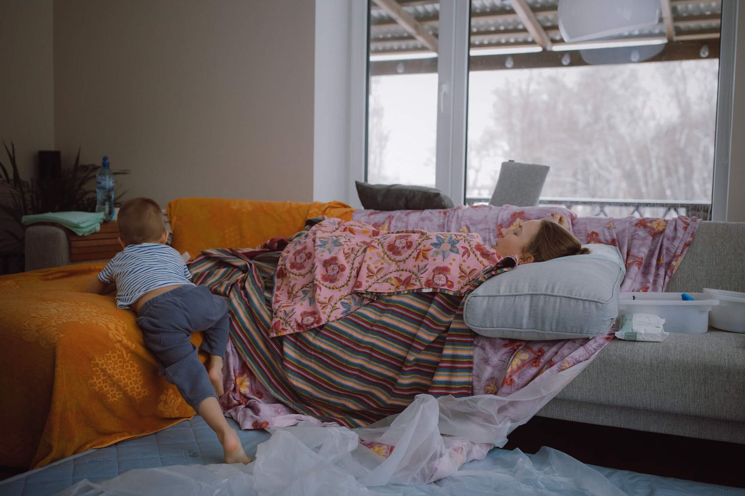 Person resting on a bed in a sunlit room with floral bedding.