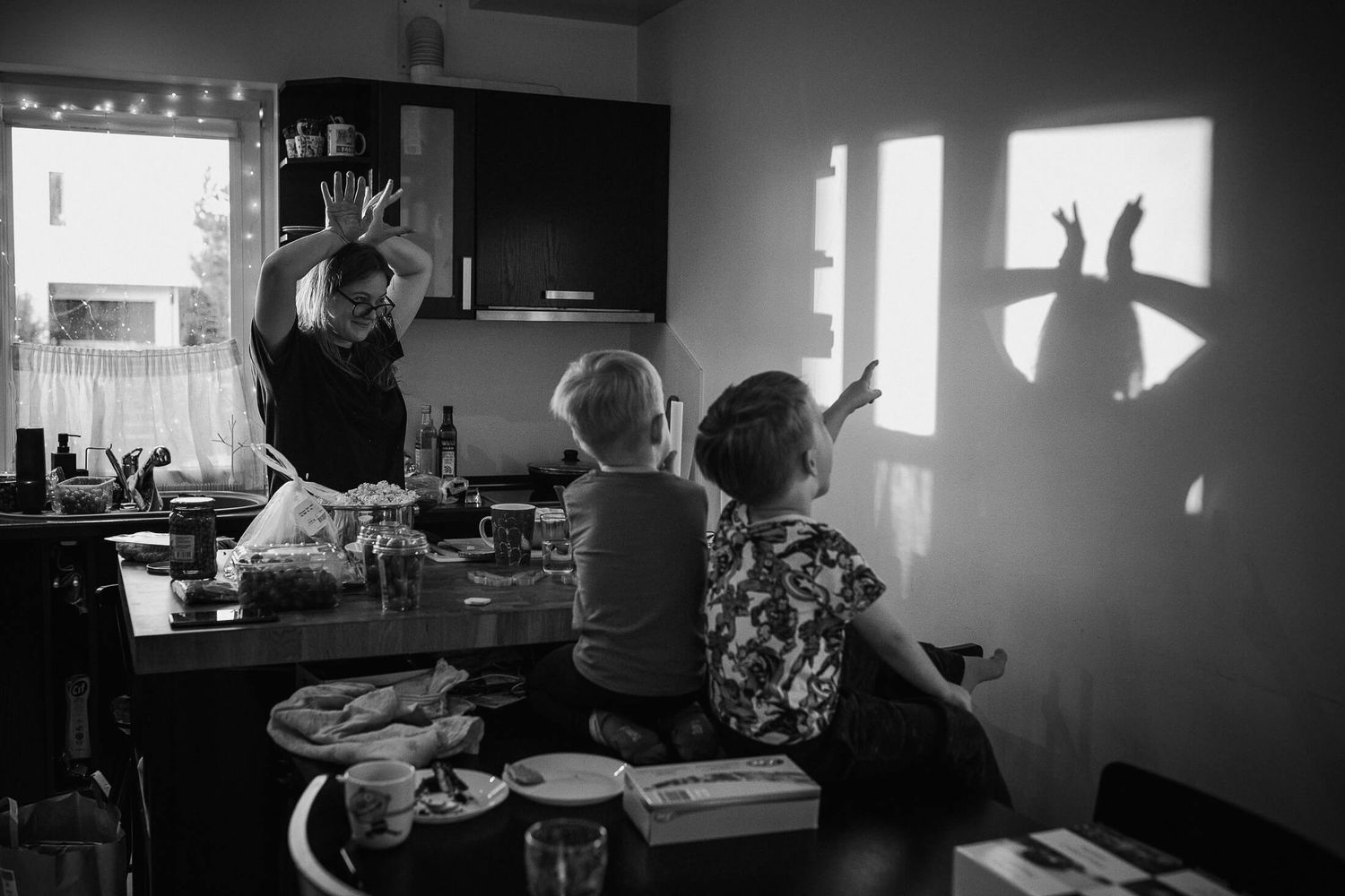 Dark silhouettes of people in a dimly lit room with windows casting dramatic shadows.