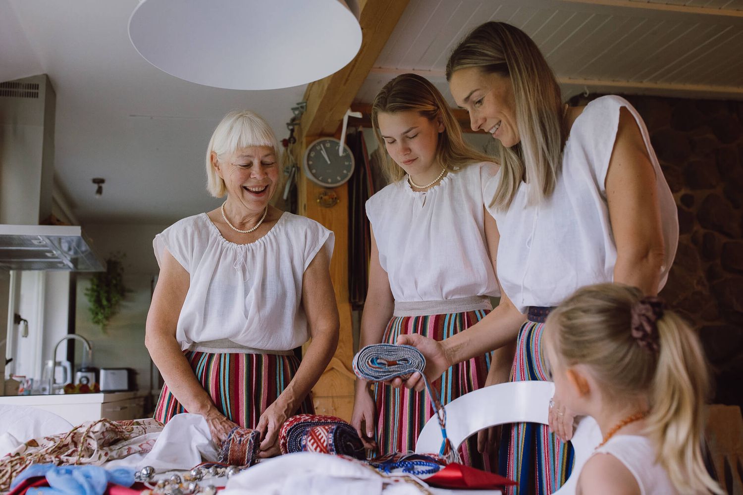 Three generations of women in matching folk costumes with striped skirts gather around a table laughing.