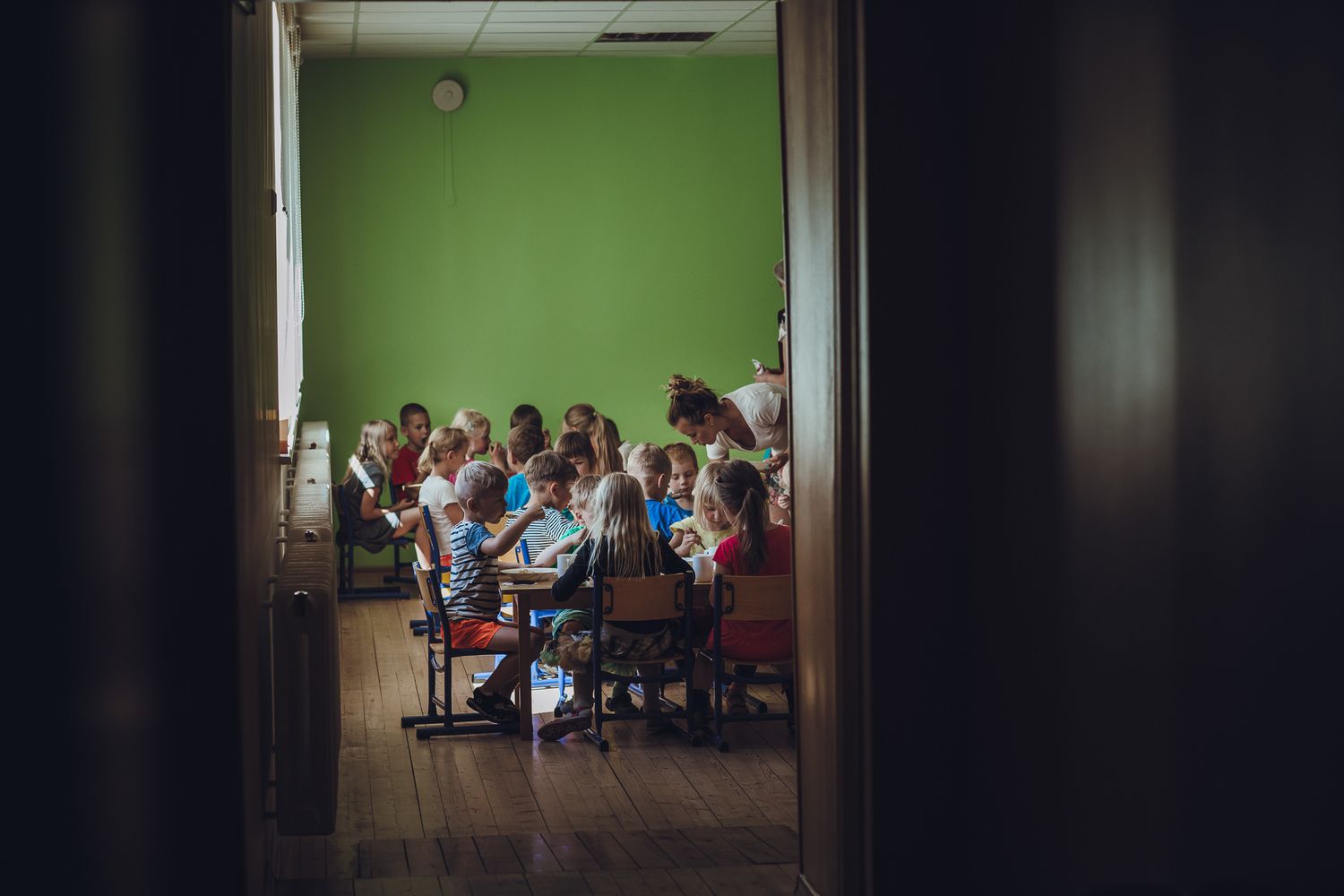 Students gathered in a classroom with green walls viewed through a doorway.