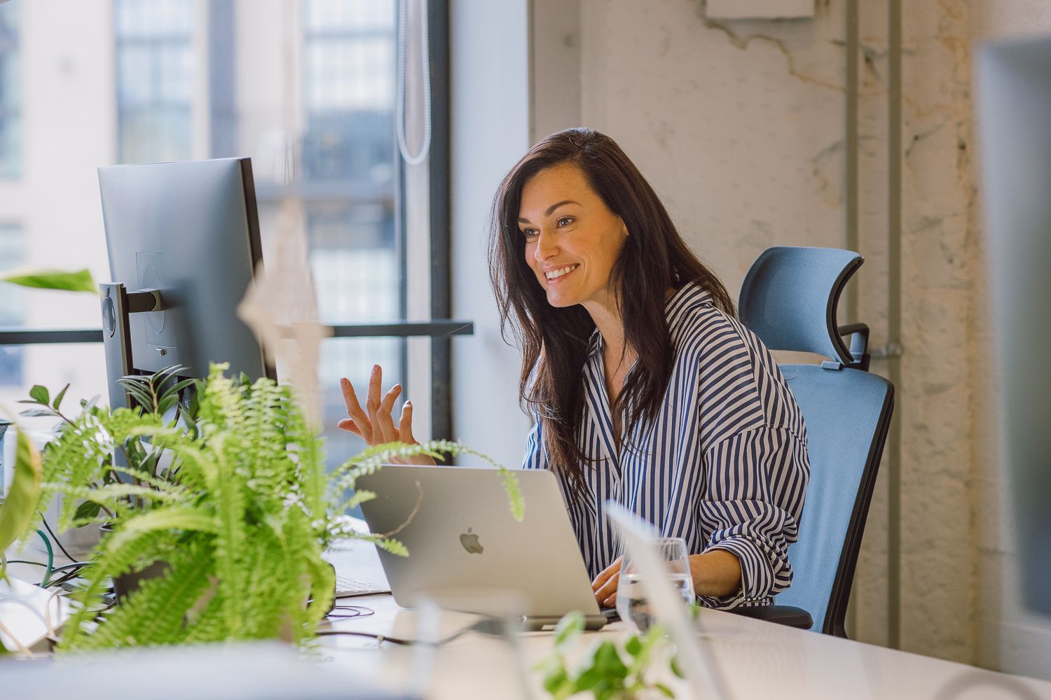 Professional working at modern office desk with plants and computer setup.