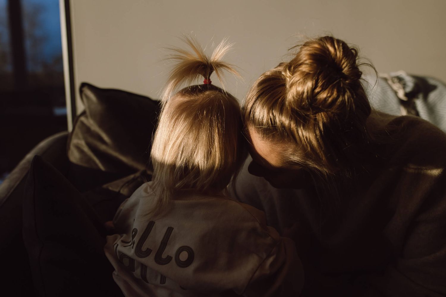 Two people with buns in their hair sitting together on a dark couch.