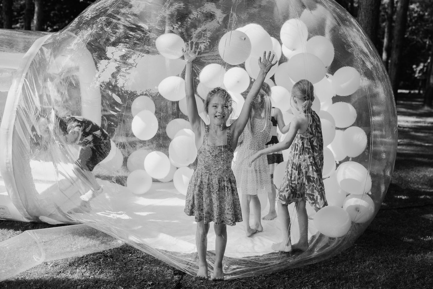 Children playing inside a large bubble installation with white balloons.