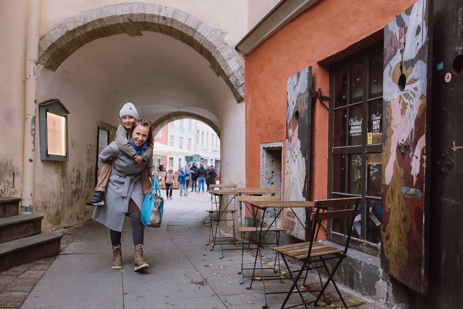 Stone archway passage in historic European city street with pedestrians walking.