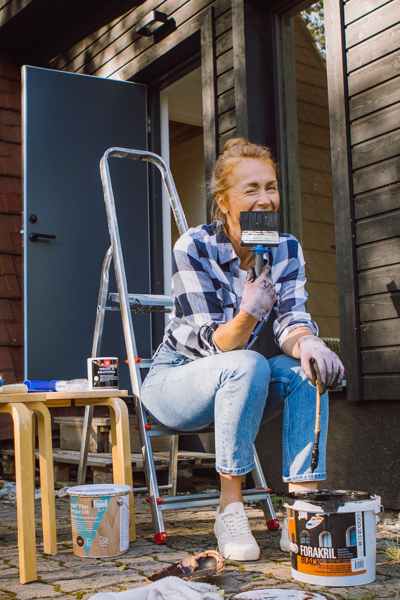 Someone in casual wear sits on wooden steps with painting supplies nearby.