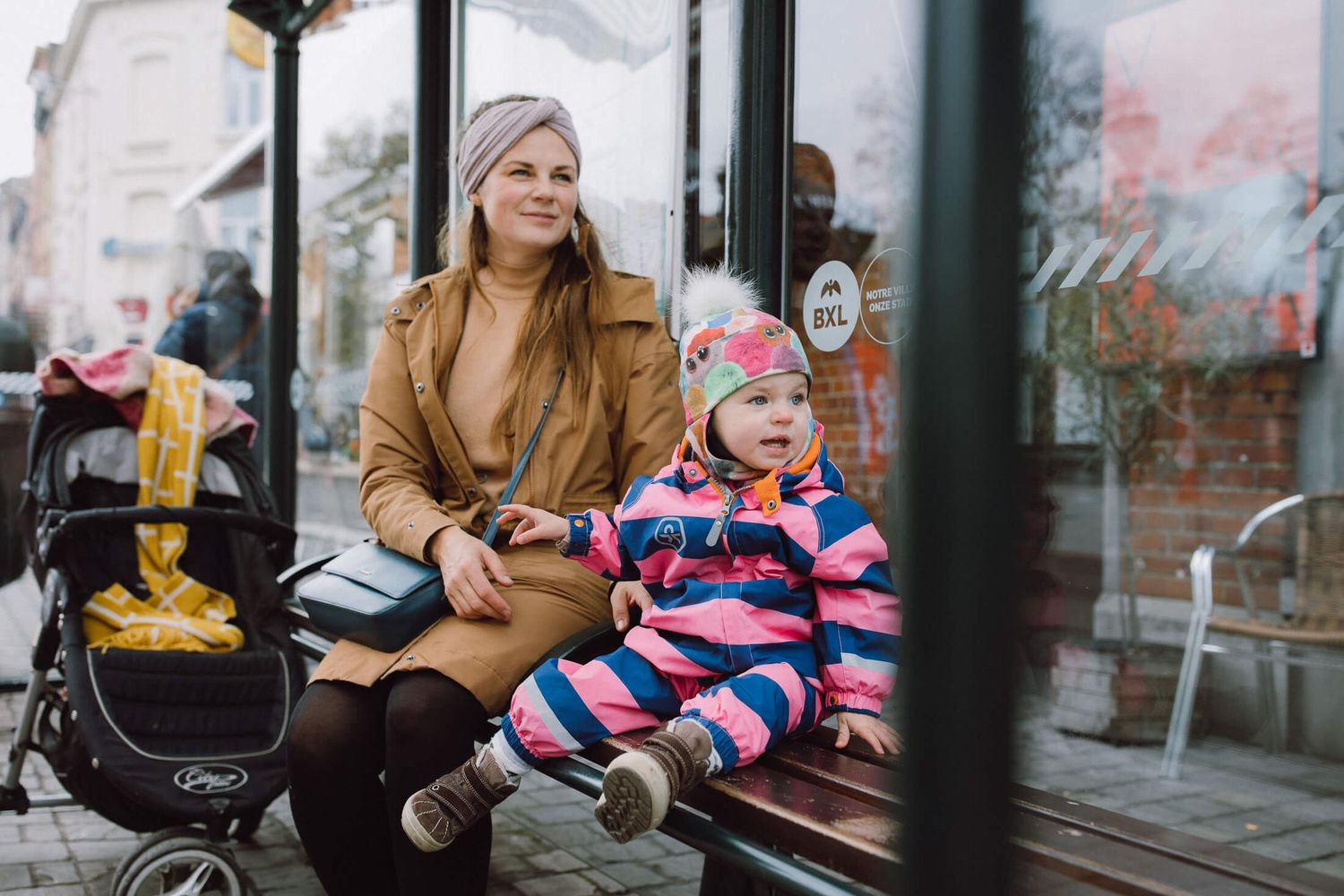 People sitting at a transit station with glass walls and winter clothing.