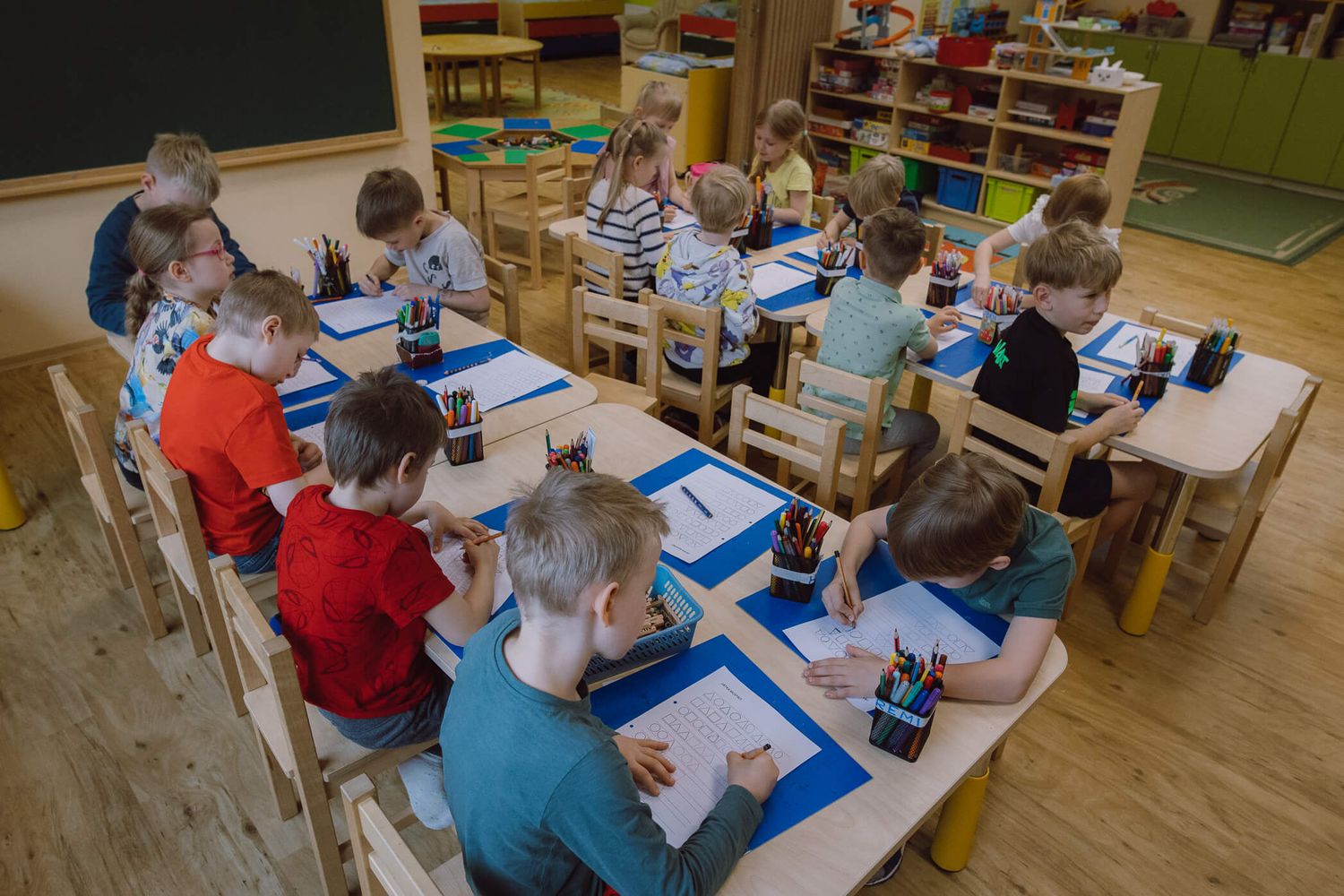 Students sit at tables working on educational activities in a bright classroom setting.