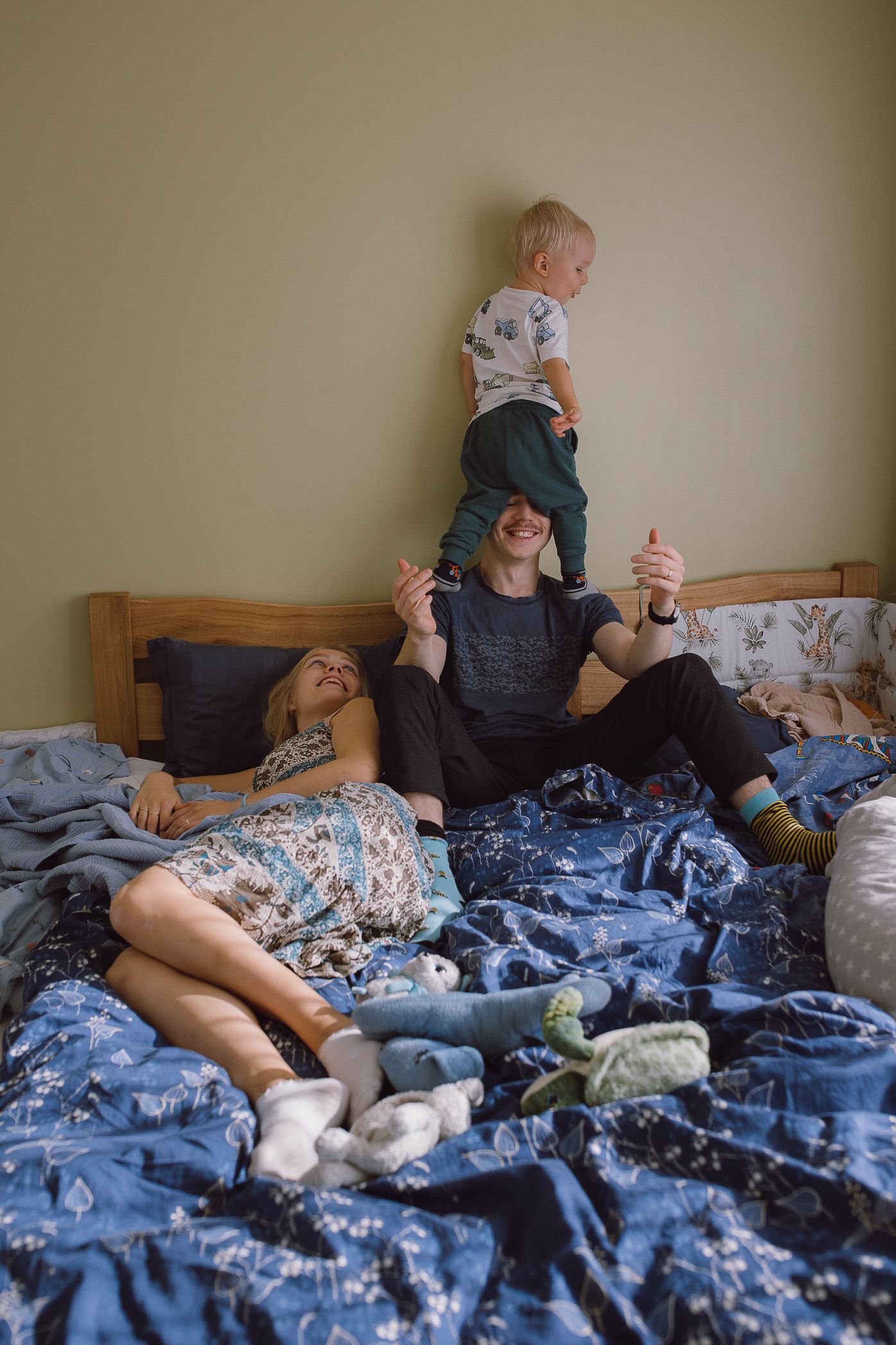 Child and parent relaxing together on blue patterned bedding with stuffed animals.