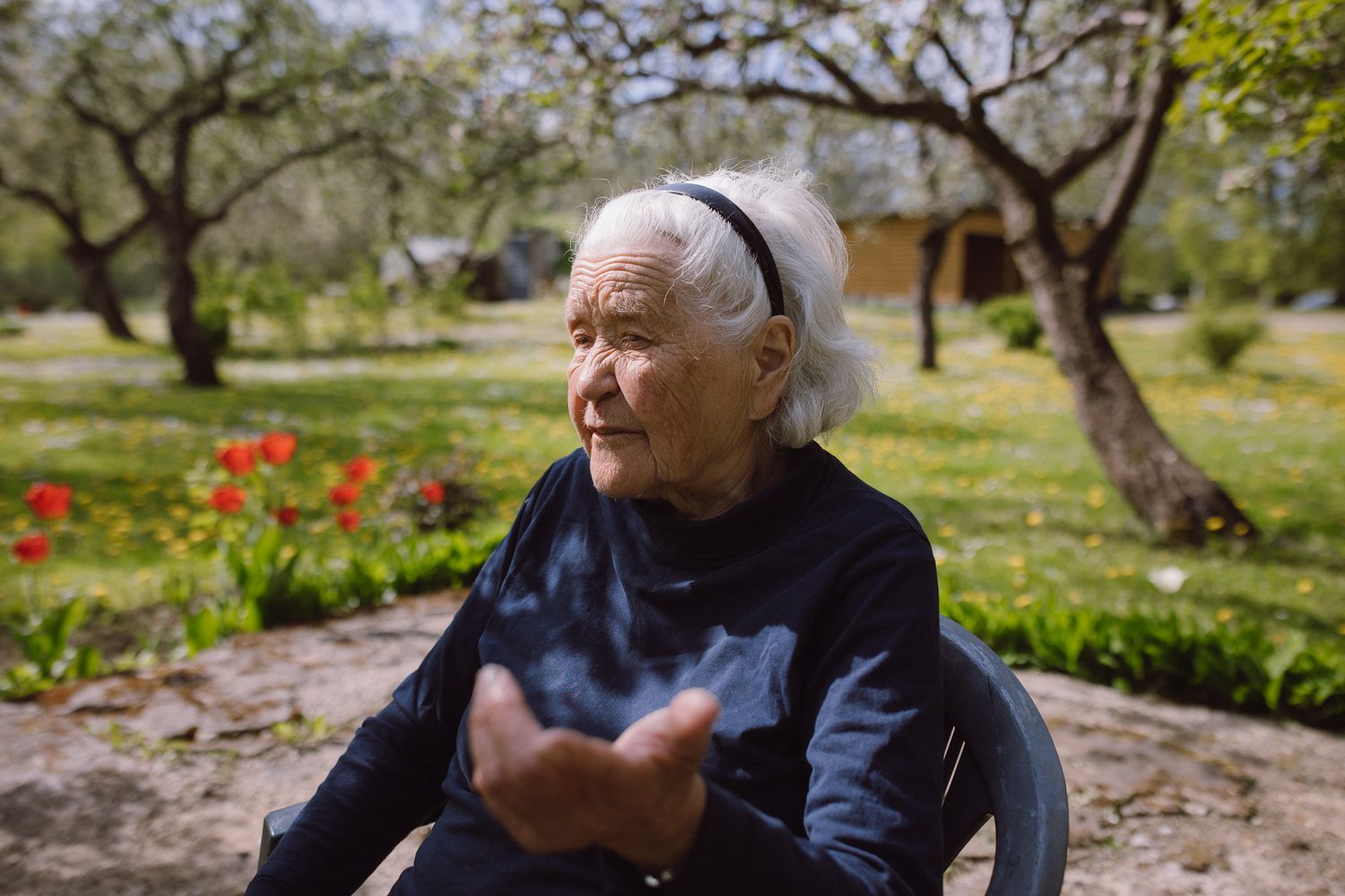 A person sits on a bench in a garden surrounded by blooming red tulips and spring foliage.