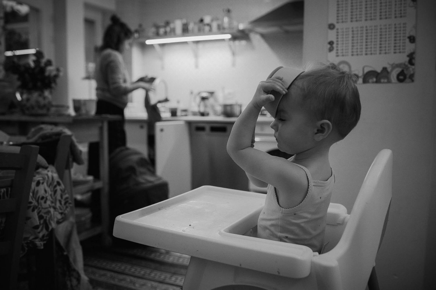 A child sits in a high chair in a kitchen setting captured in black and white.