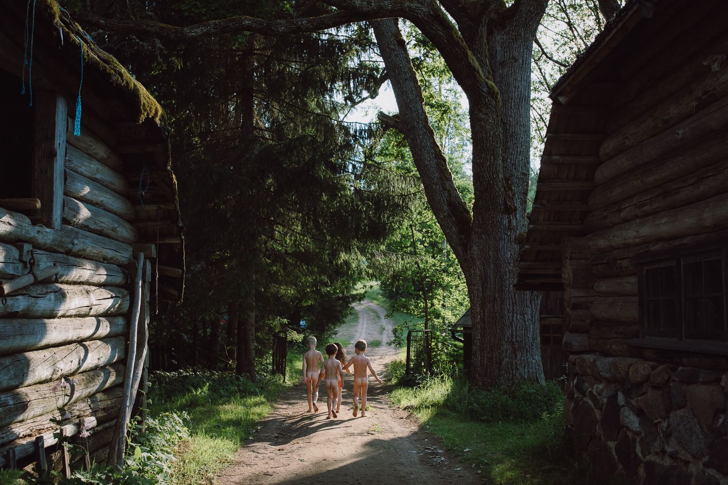 People walking down a shaded path between rustic wooden buildings.