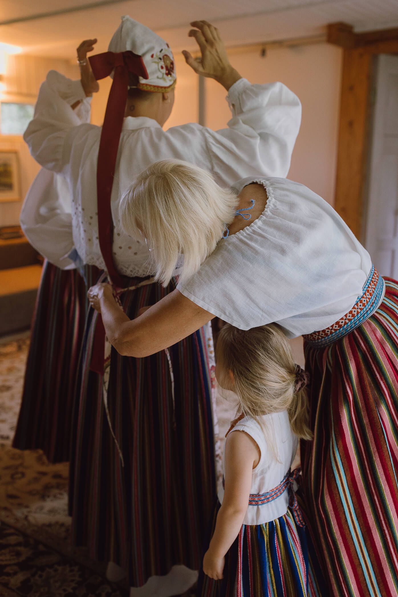 Women and child in traditional folk costumes with embroidered skirts and white blouses during a cultural ceremony.