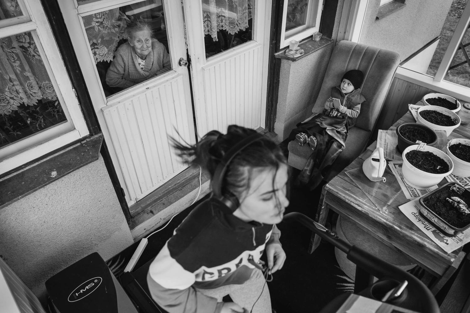 Black and white interior scene showing people in a cozy room with photographs on the wall.