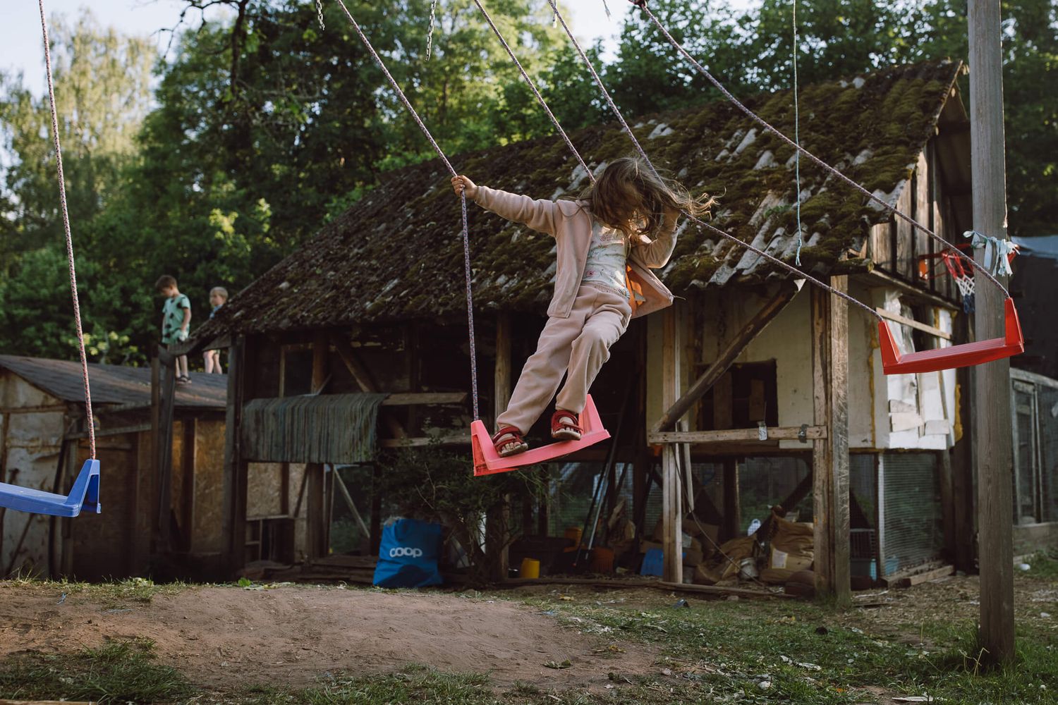 Children playing on rope swings in a backyard with trees and outdoor equipment.