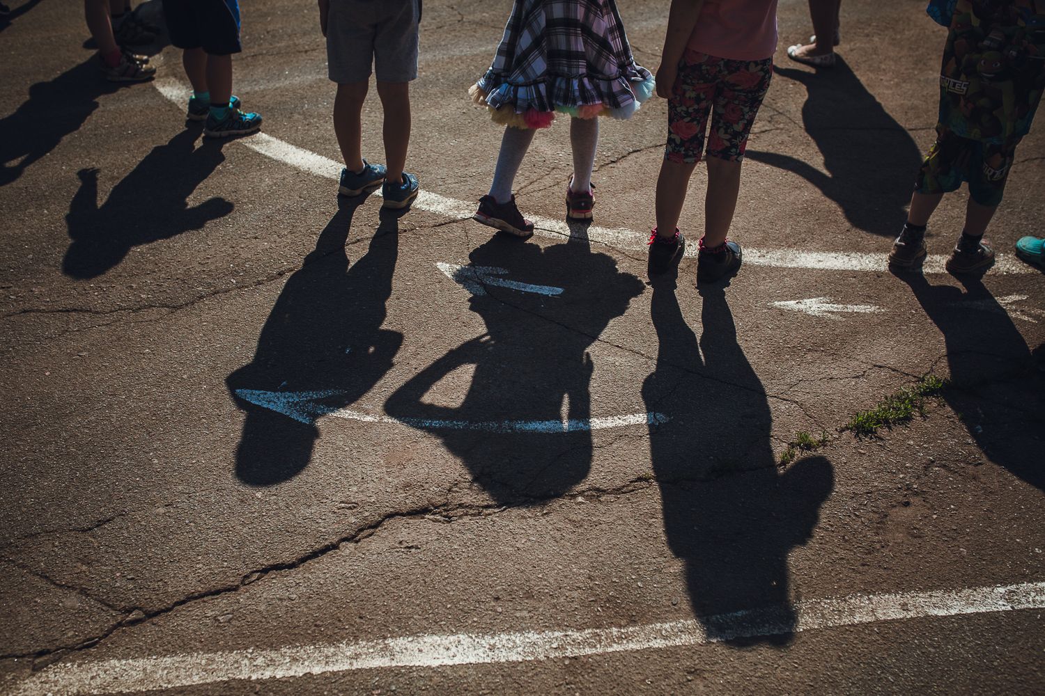 Shadows of people cast on pavement with white line markings.