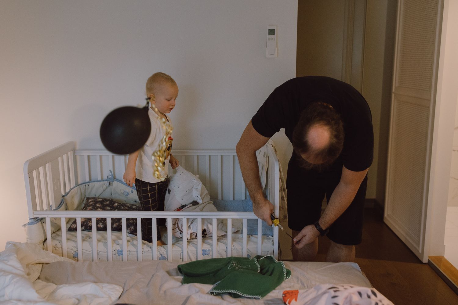 White crib in bedroom with people gathered around during daily routine.