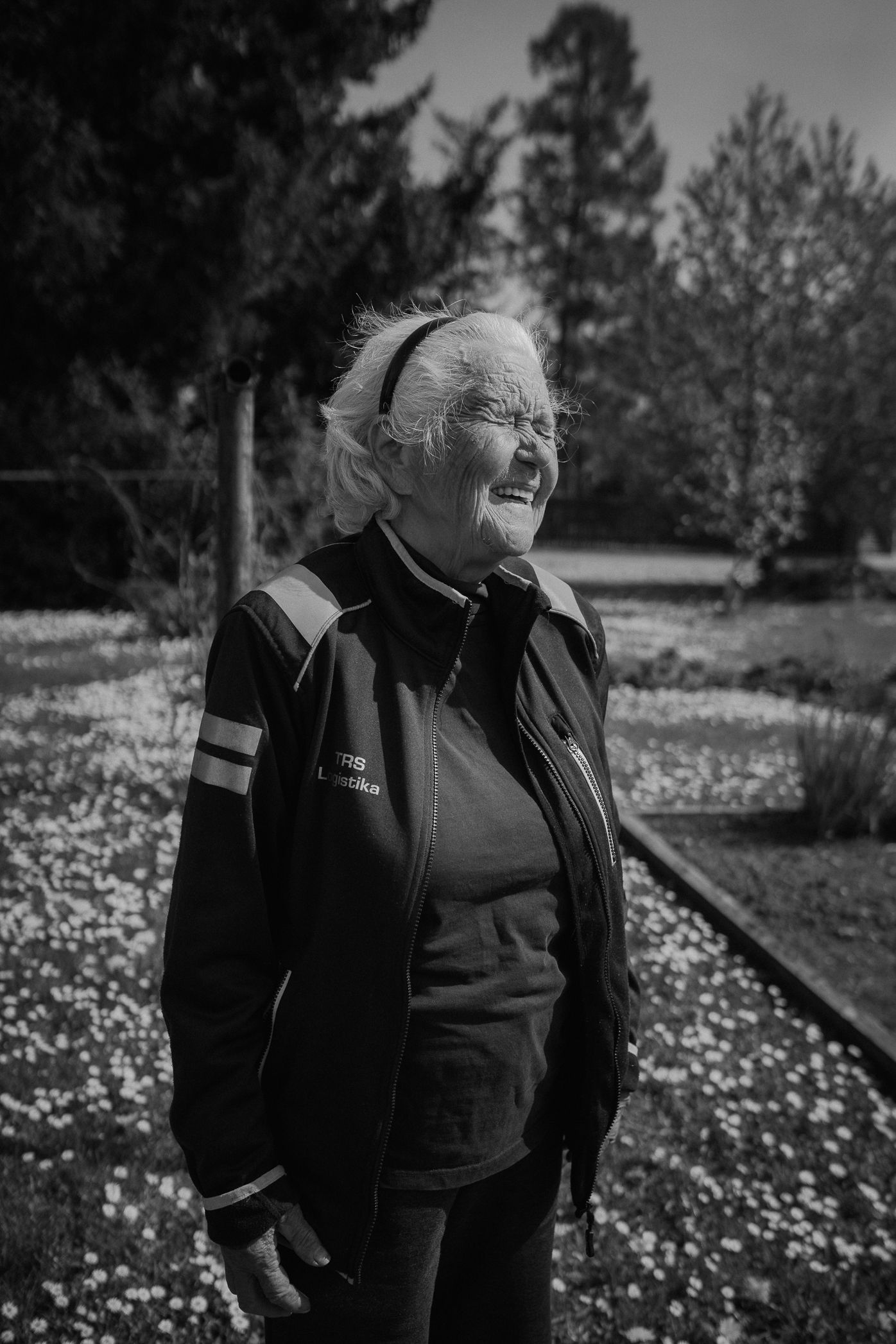 Black and white portrait of a person in dark clothing standing in a field of wildflowers on a sunny day.