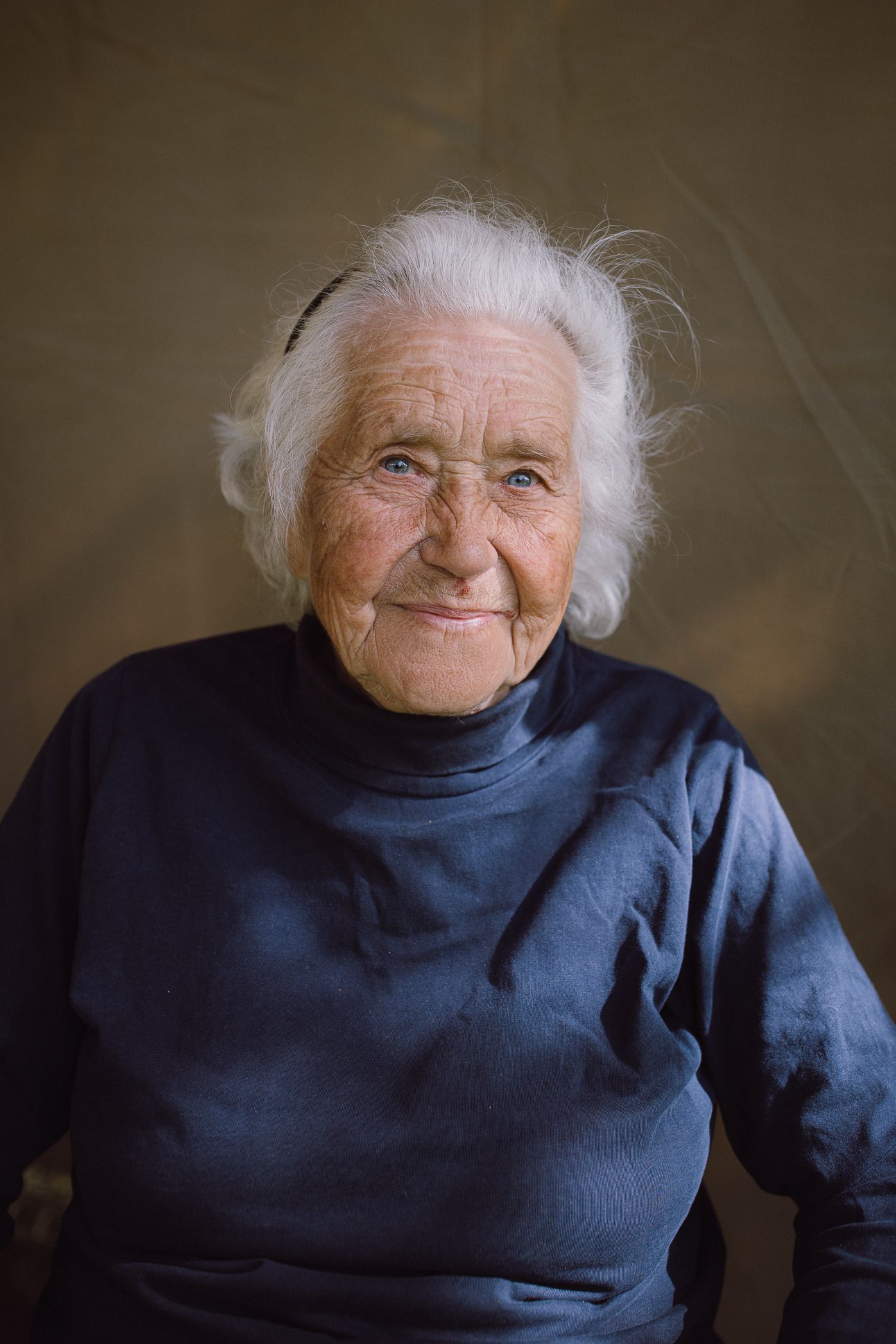 An elderly person wearing a navy blue sweater smiles warmly in a series of candid portrait shots.
