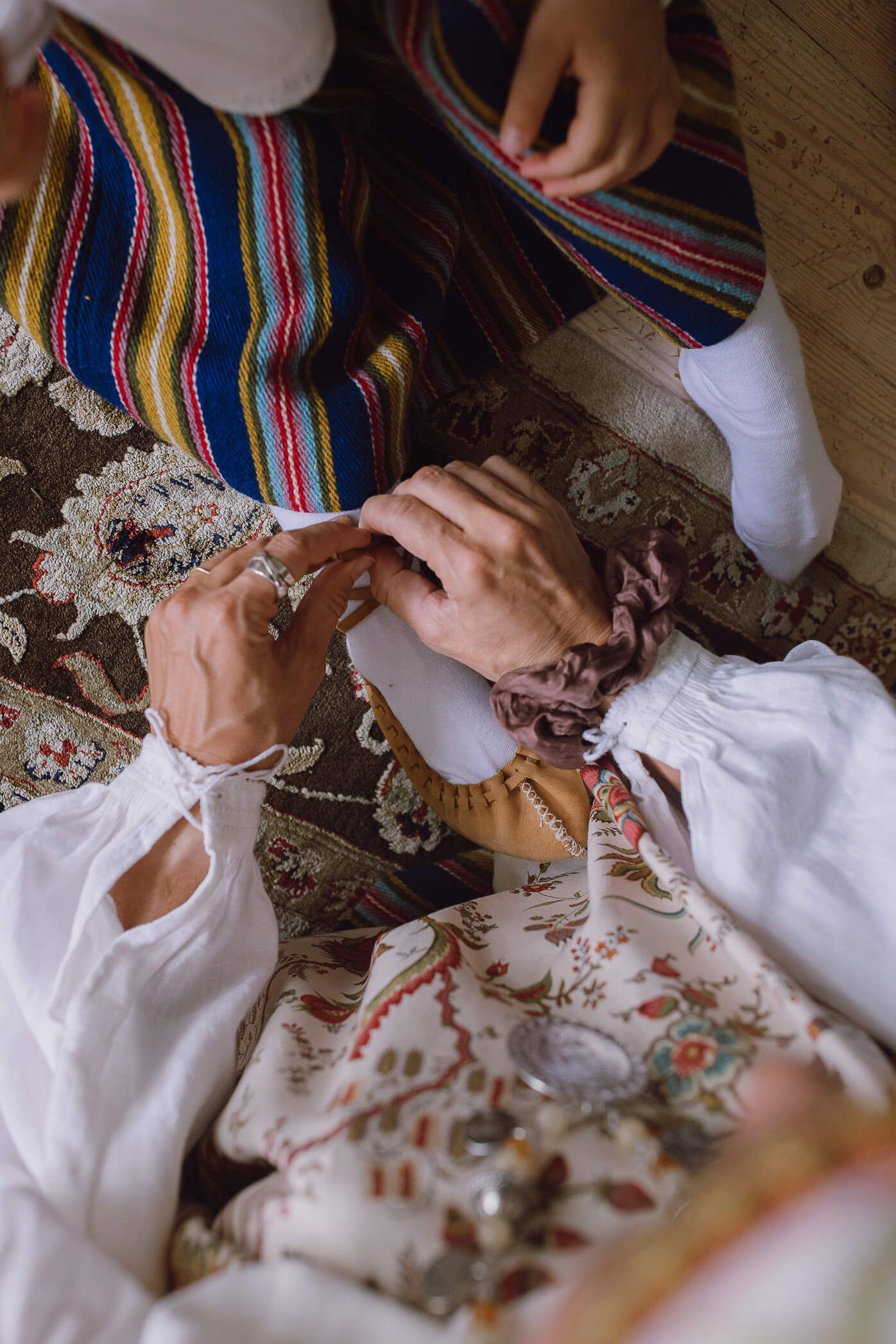 Person in traditional folk costume being dressed, with embroidered garments and colorful striped fabric visible.