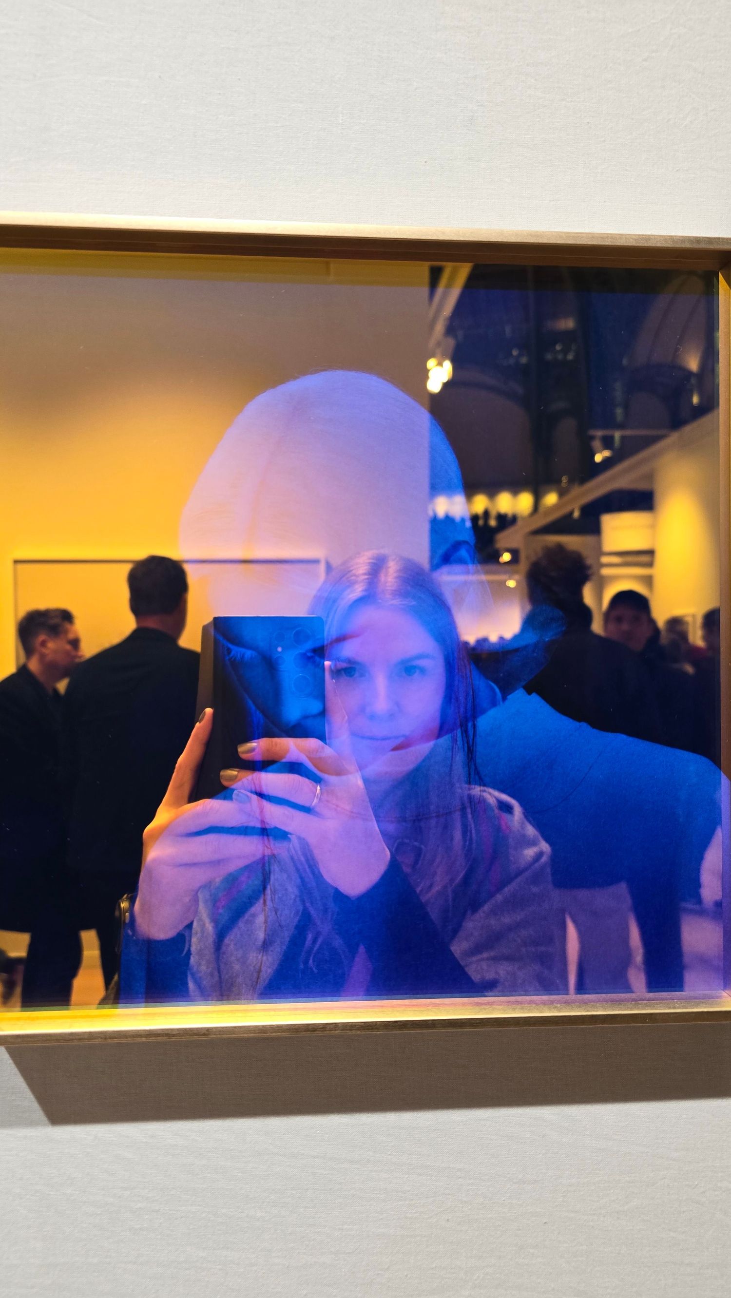 A mirror reflection in a dimly lit room with warm yellow and blue ambient lighting.
