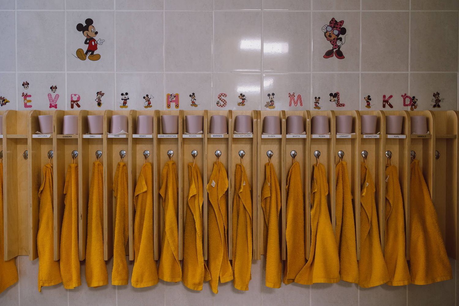 A row of yellow Mickey Mouse plush toys hanging on display hooks along a retail store wall.